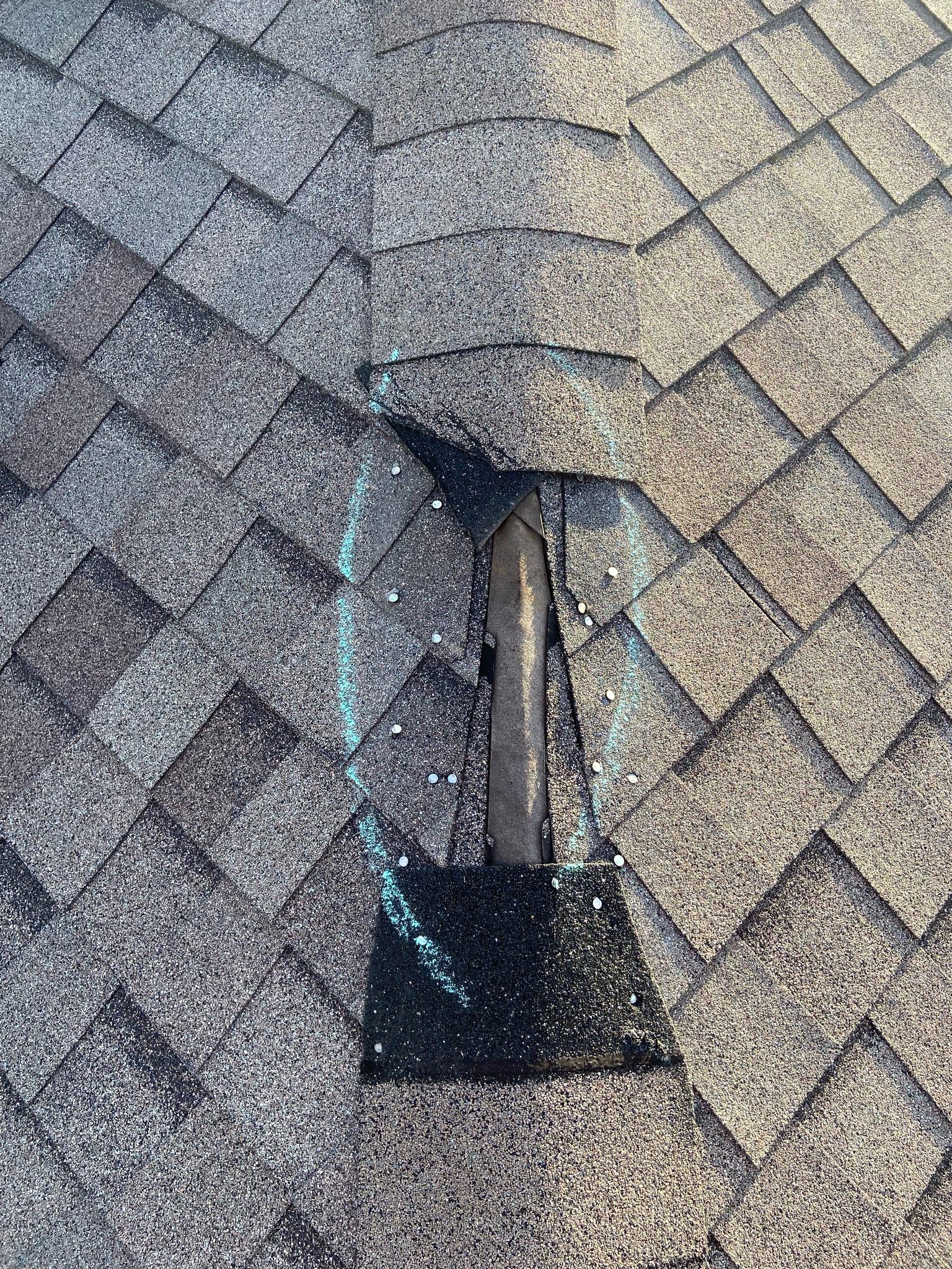 Damaged roof shingles exposing underlayment, with the area marked by a blue chalk circle.